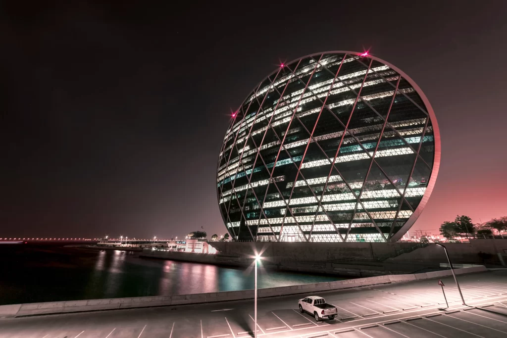 Современное здание штаб-квартиры строительной компании Aldar в ночном свете в Абу-Даби, ОАЭ
