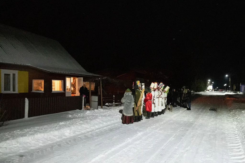 Цари-солдаты и другие персонажи обряда "Калядныя цары" ожидают угощения у дома хозяина, Семежево, Беларусь